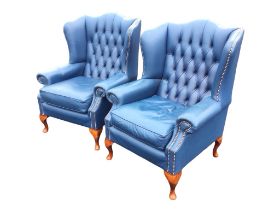A pair of leather wing armchairs with button upholstered backs and outscrolled arms with brass