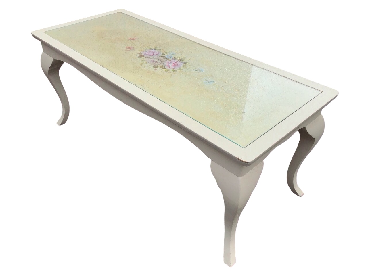 A painted coffee table with rectangular top decorated with a floral spray under glass, above a