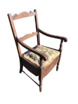 An Edwardian hardwood armchair with shaped fan carved rails to back above an upholstered commode