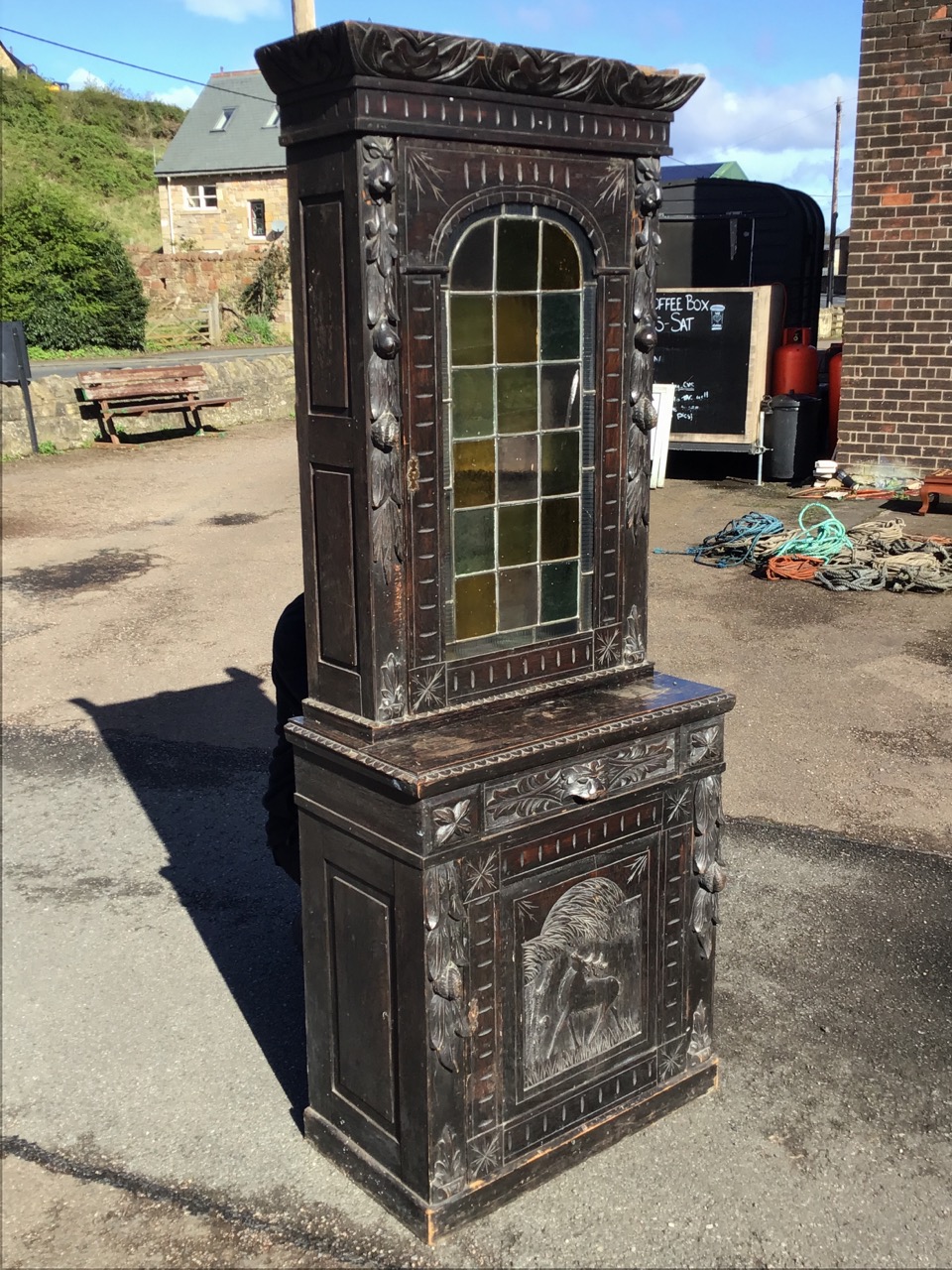A Victorian oak carved cabinet with leaf carved cornice above an arched leaded glass door flanked by