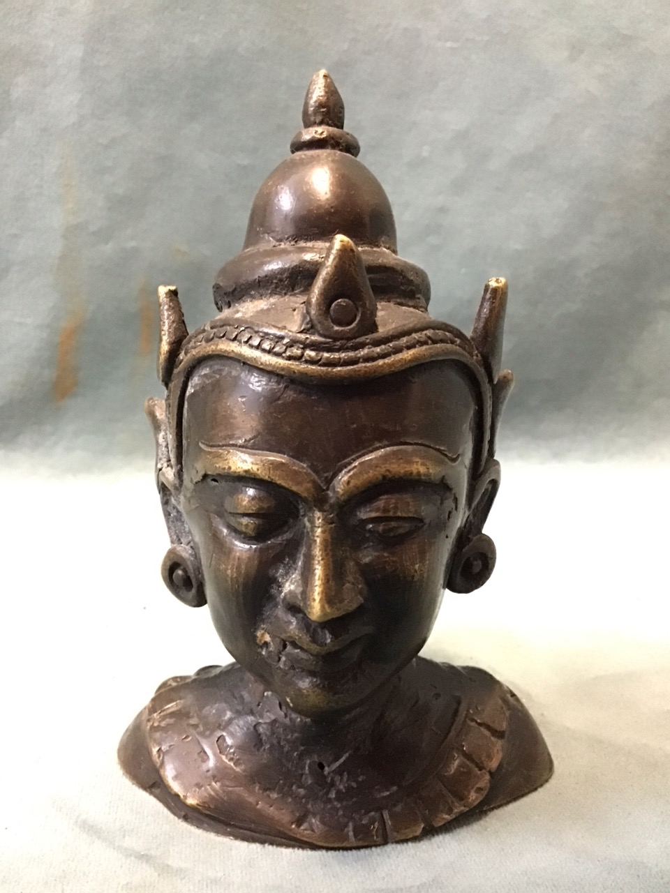 A small Burmese patinated brass bust of a buddhist deity with a serene expression wearing an