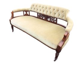 A Victorian walnut sofa with button upholstered back and rounded arms on carved pierced splats,