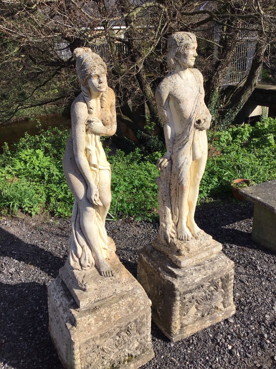 A pair of classical composition stone garden statues with a draped couple standing by logs on square - Image 2 of 3