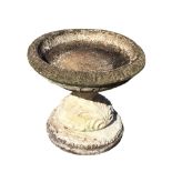 A squat composition stone garden birdbath with circular ribbed bowl on waisted leaf moulded