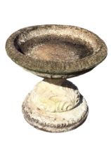 A squat composition stone garden birdbath with circular ribbed bowl on waisted leaf moulded