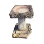 A composition stone garden birdbath with square bowl on tapering roughcast panelled column above a