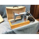 A 50s cased Atlas electric portable sewing machine, with bakelite foot pedal on a beech base, the