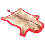 An animal skin rug on red baize ground. (59in x 96in)