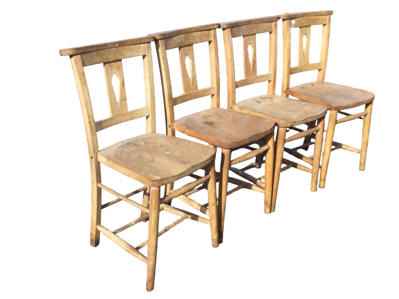 A set of four beech and elm church chairs with shaped flat backs and pierced splats above solid