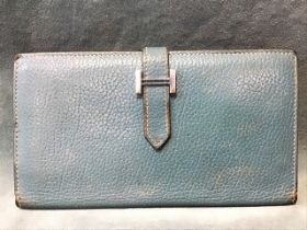 A pale blue Hermès leather wallet with four pouches and a zip compartment, having metal H clasp.