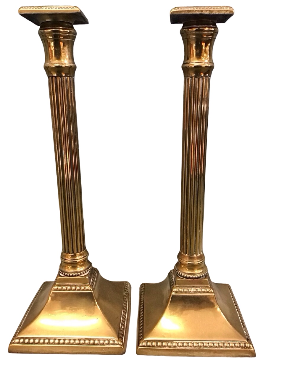 A pair of Georgian brass candlesticks with square beaded sconces above reeded Tuscan columns on