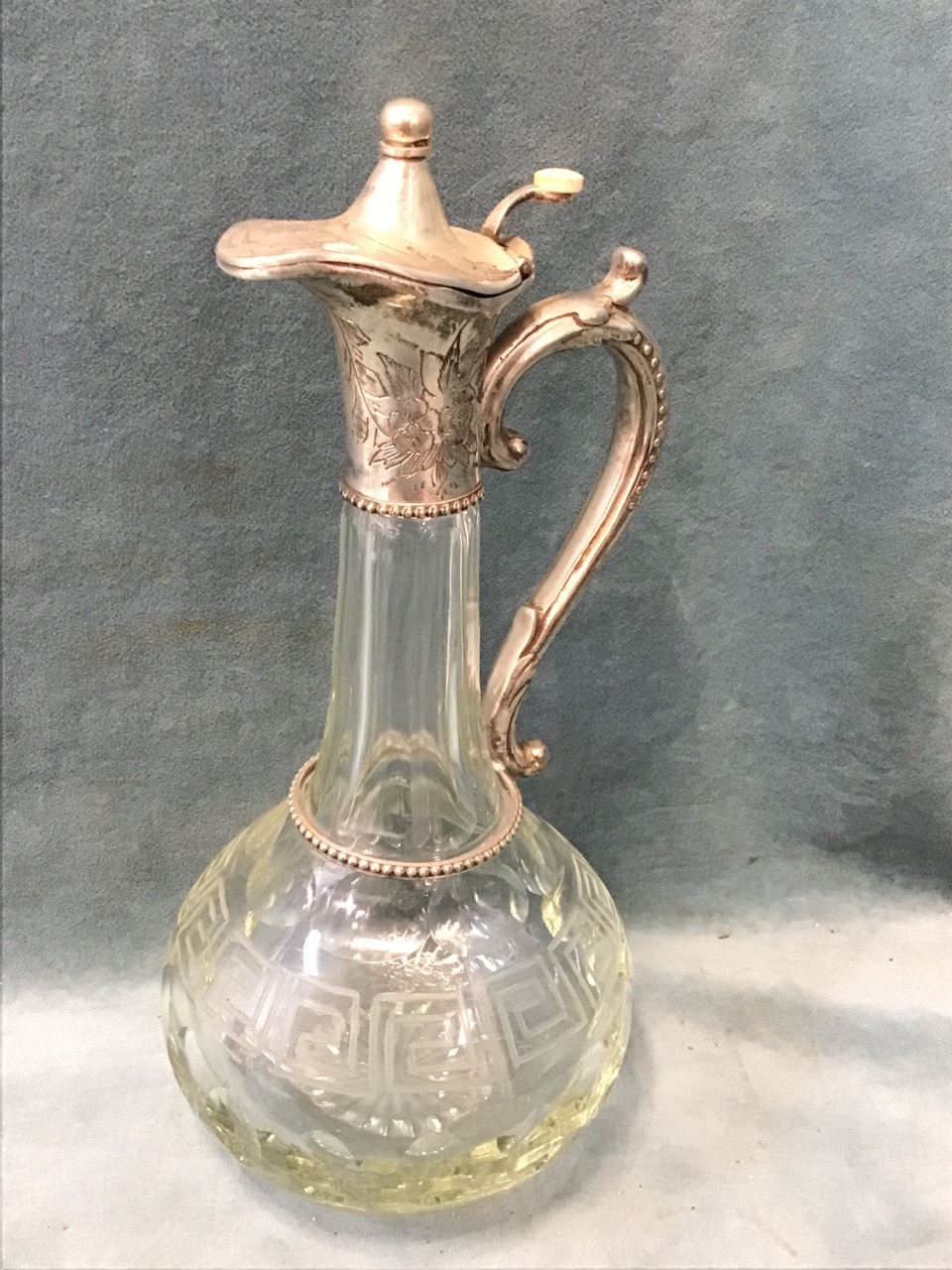 A cut glass globular claret jug with porthole and greek key motifs, having floral engraved silver