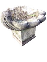 A composition stone shell cast birdbath mounted on an associated square fluted column support. (