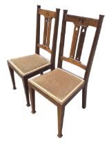 A pair of Edwardian art nouveau oak chairs with pierced crestrails and twin splats above upholstered