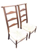 A pair of country ladderback chairs, the shaped flat top backs above arched rails and rush seats,