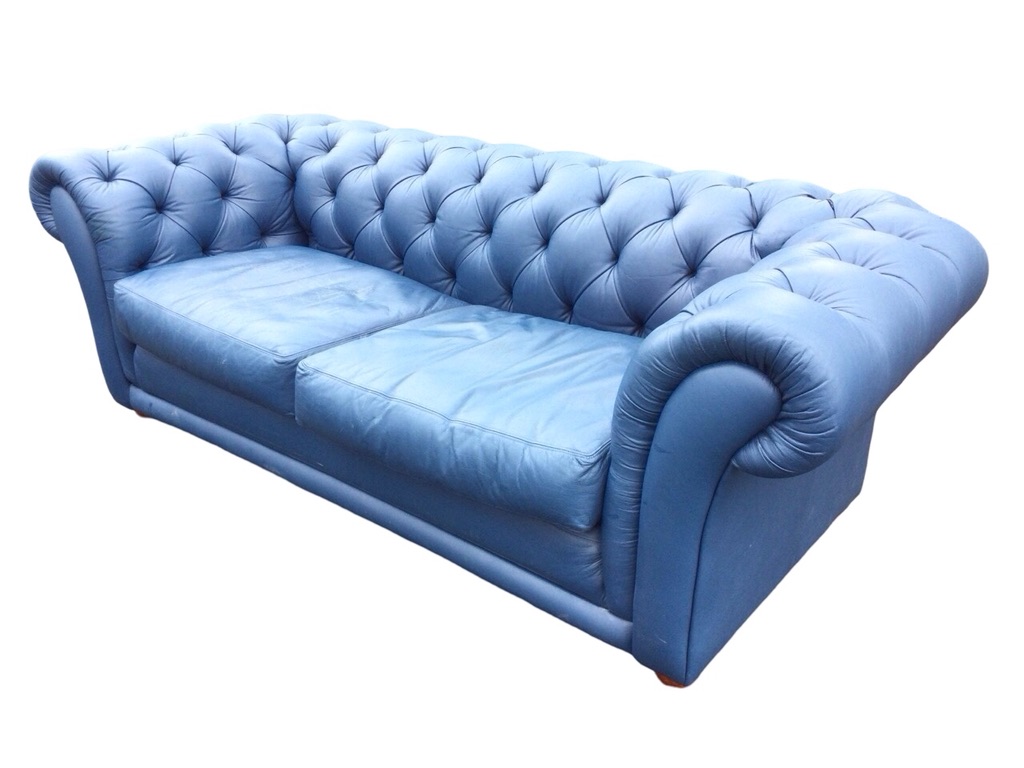 A leather button upholstered chesterfield sofa with loose cushions and padded apron, raised on bun