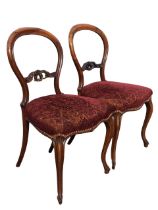 A pair of Victorian rosewood balloon back chairs with foliate carved pierced rails above upholstered