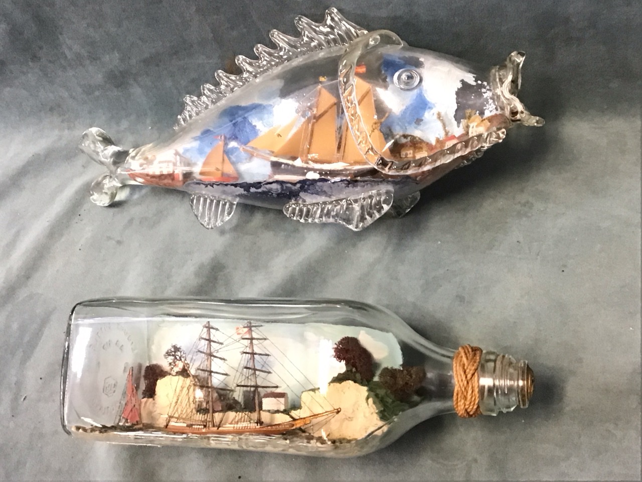 A ship in a bottle diorama with two sailing boats below a clifftop village in a square bottle -