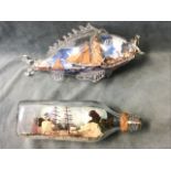 A ship in a bottle diorama with two sailing boats below a clifftop village in a square bottle -