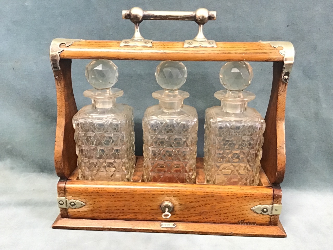 A late Victorian oak tantalus with silver plated mounts, the square cut glass decanters with ball