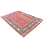 A Tekke style oriental rug woven with grid of oval floral medallions on red ground, framed by border