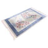 A rectangular Chinese wool rug with asymmetrical peony and blossom motifs on a pale blue ground