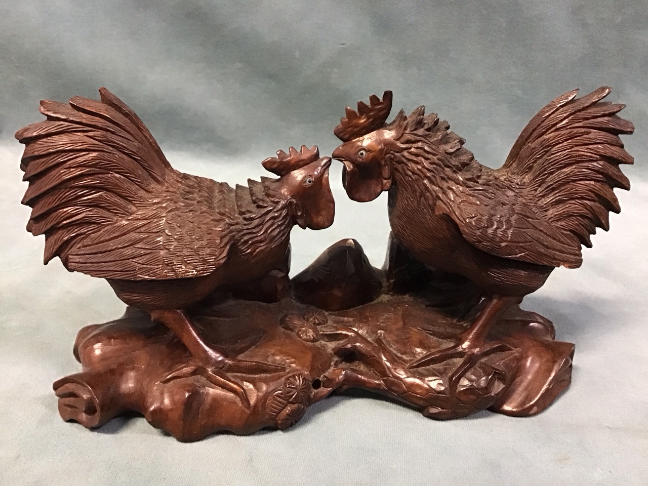 A Chinese carved hardwood figure of two duelling cockerels with glass inset eyes, on a