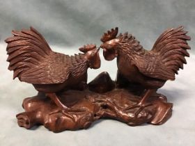 A Chinese carved hardwood figure of two duelling cockerels with glass inset eyes, on a