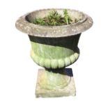 A composition stone classical garden urn with moulded rim on lobbed body, raised on socle with