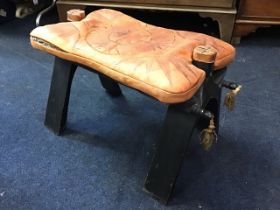 An Eastern camel saddle stool with loose leather cushion seat on a hinged folding hardwood frame,