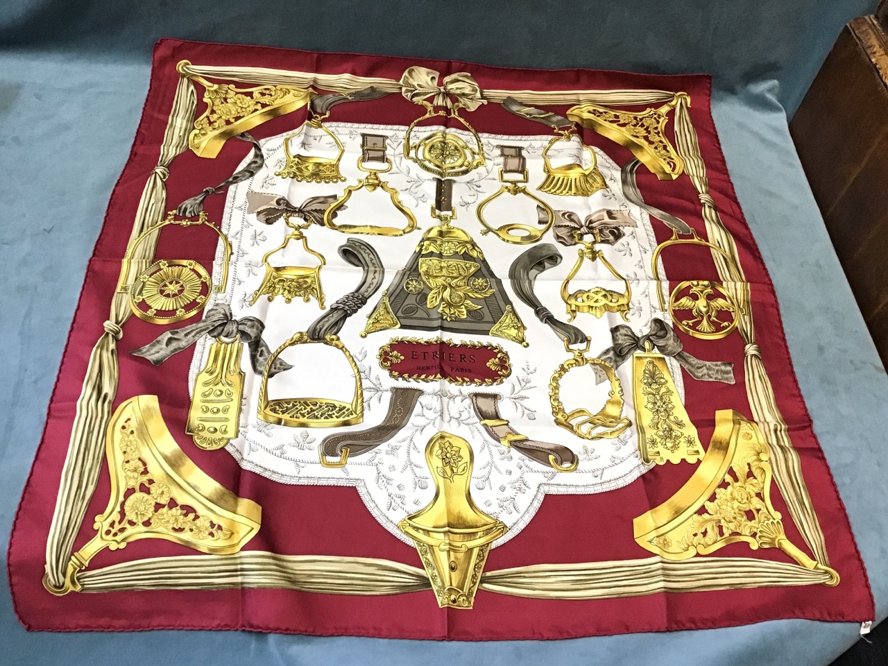 A silk Hermès scarf depicting a bell surrounded by various ornate stirrups, having deep red