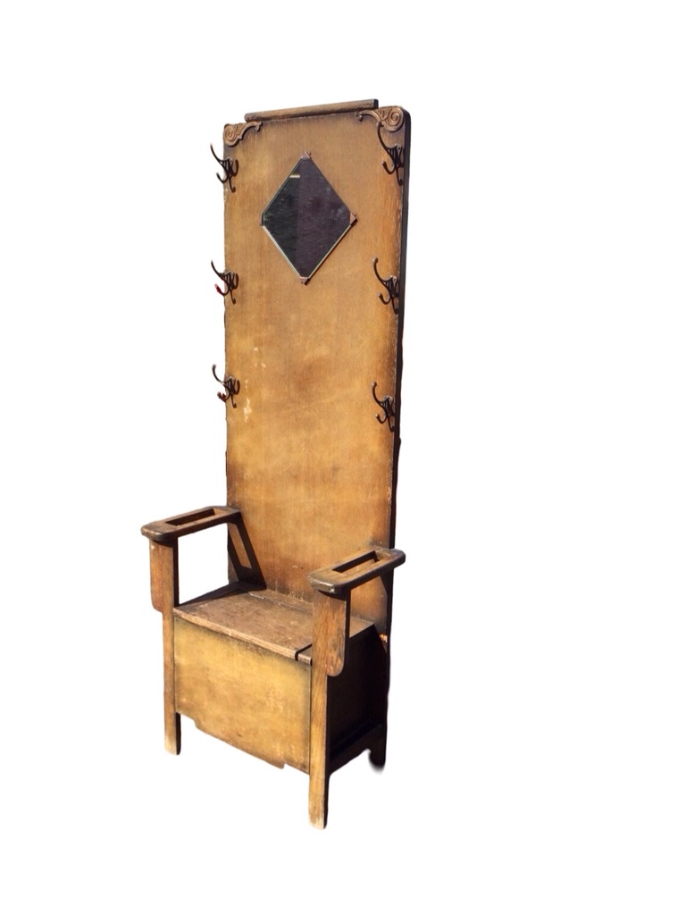 A 1930s oak hallstand with applied scrolled carving and six pegs to back, above a seat with hinged