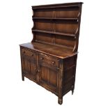 An Ercol elm dresser with moulded cornice and open shelves flanked by shaped sides, above a