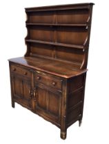 An Ercol elm dresser with moulded cornice and open shelves flanked by shaped sides, above a