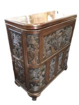 An oriental hardwood cocktail cabinet profusely carved with panels of figures in landscapes with