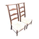 A pair of country ladderback chairs, the shaped flat top backs above arched rails and rush seats,