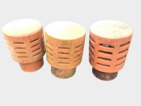 Three terracotta chimney cowls of tubular form with domed tops above slit-vented bodies. (13.5in) (