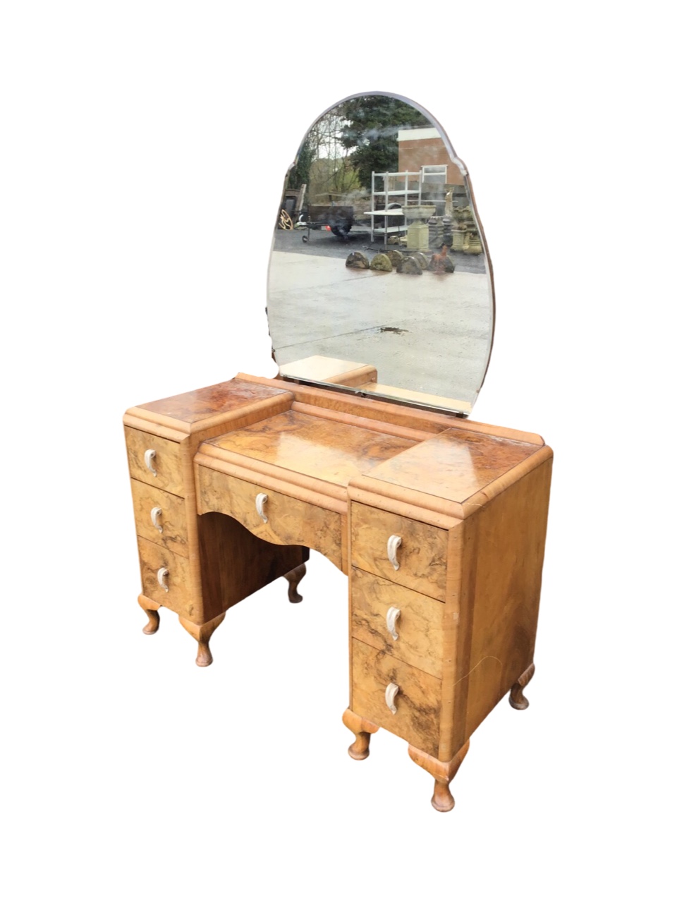 A deco walnut dressing table with cloud shaped mirror above a kneehole cabinet with shaped frieze