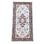 A Kashmir style wool rug with central scrolled medallion on a pale blue ground with conforming