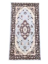A Kashmir style wool rug with central scrolled medallion on a pale blue ground with conforming