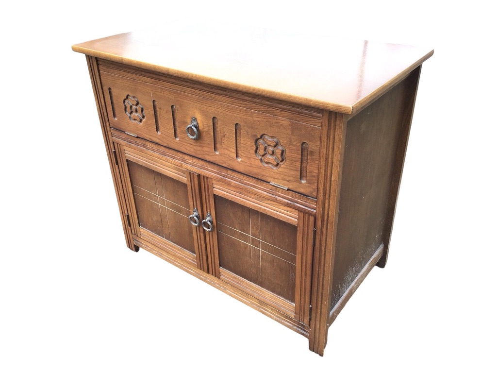 An oak cabinet with drop-down front compartment carved with fluting and flowerheads, above