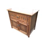 An oak cabinet with drop-down front compartment carved with fluting and flowerheads, above