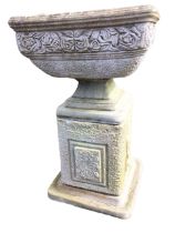 A square composition stone urn cast with frieze of roses above mottled body, supported on a square