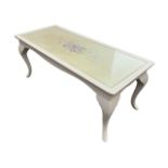 A painted coffee table with rectangular top decorated with a floral spray under glass, above a