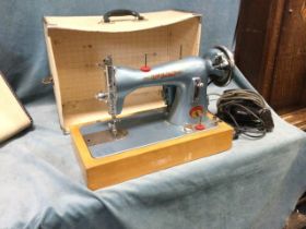 A 50s cased Atlas electric portable sewing machine, with bakelite foot pedal on a beech base, the