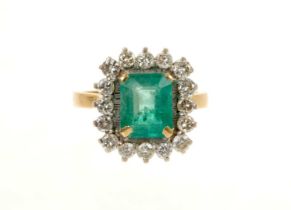 Emerald and diamond cluster ring with a rectangular step cut emerald surrounded by 16 brilliant cut