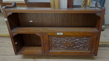 A 63cm early 20th Century carved oak wall hanging unit with two open shelves and panelled cupboard