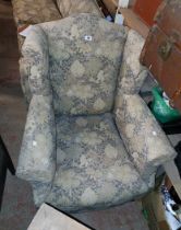 An early 20th Century wingback armchair upholstered in decorative machine tapestry, set on shaped