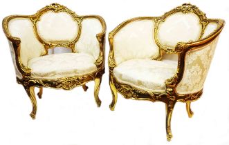 A pair of ornate reproduction giltwood show frame fauteuil tub chairs with cream coloured machine