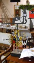 A vintage wrought iron weather vane with scroll decoration and gardener vane set on wood block